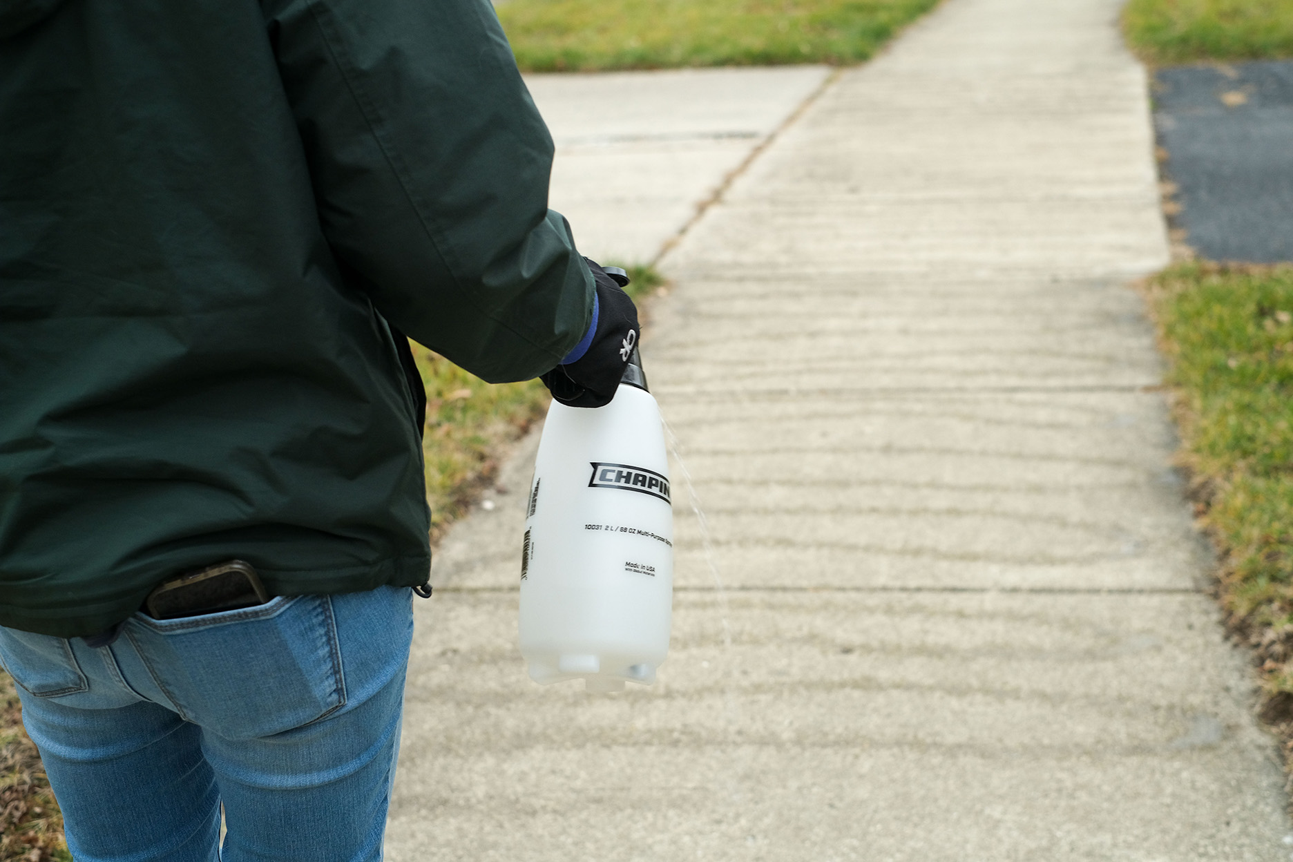 A person uses a handheld sprayer to spray brine on the sidewalk